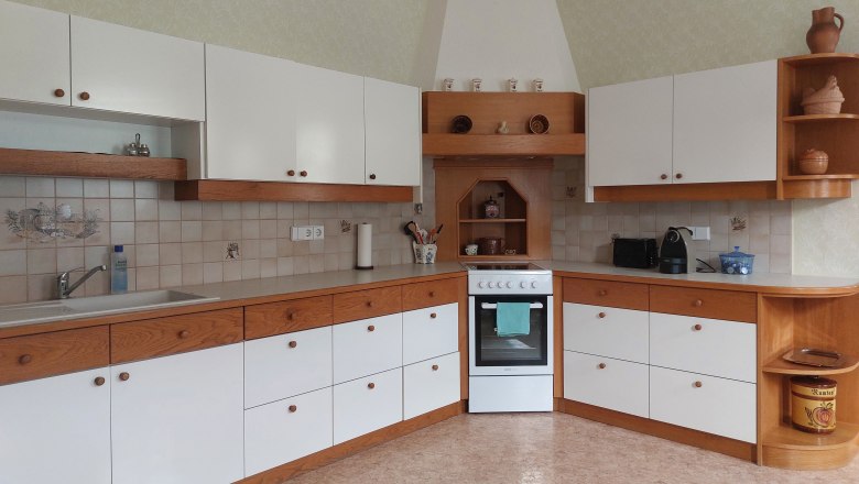 Kuchyňa s bielymi a dreven&yacute;mi skrinkami, spor&aacute;kom a drezom.