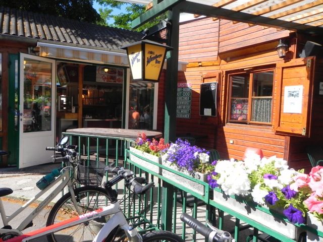 Útulný snack bar s drevenými stenami, bicyklami a rozkvitnutými kvetmi v popredí.