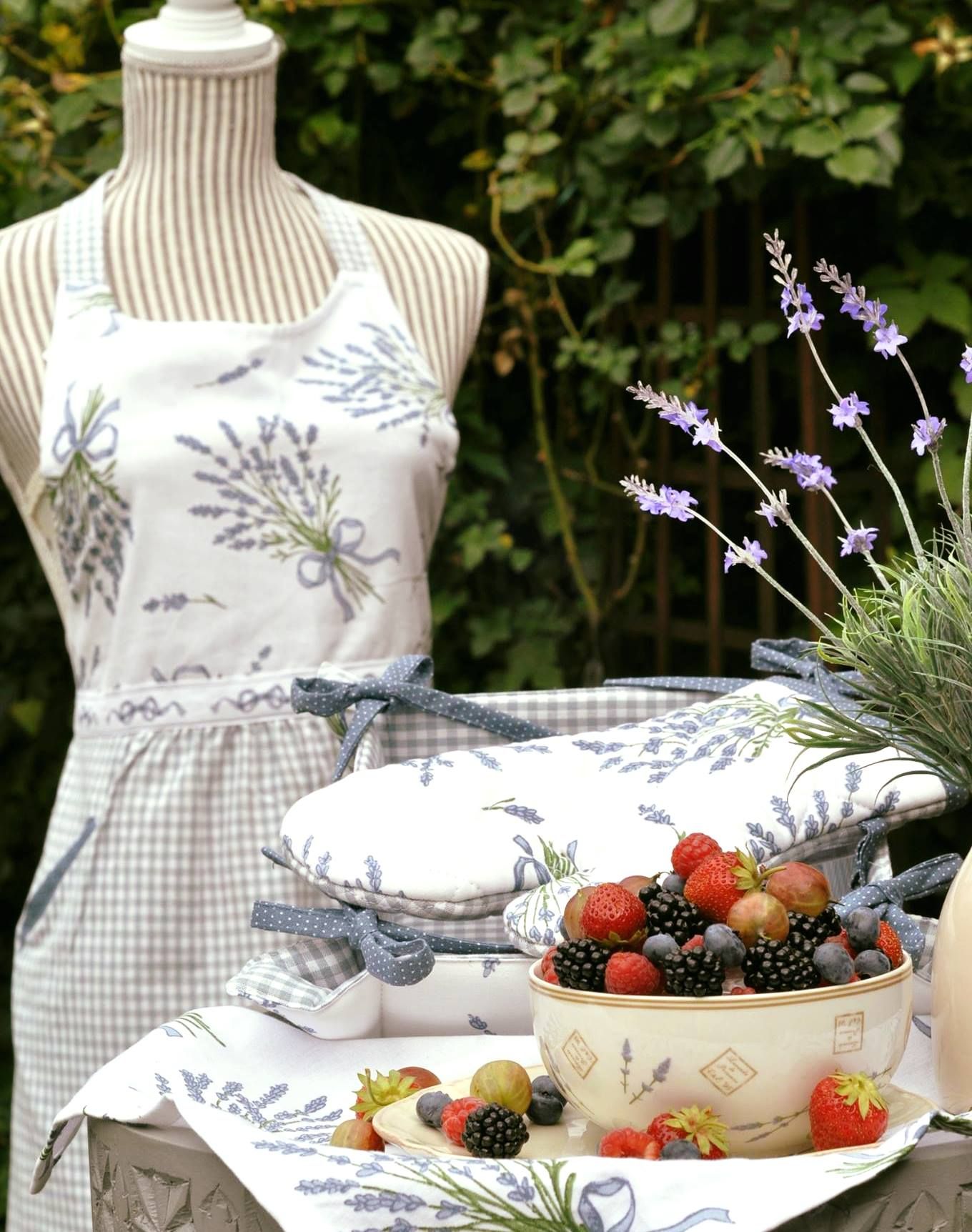 Misa s bobuľami na stole s levanduľovými dekoráciami a krajčírska figurína so zásterou v pozadí.