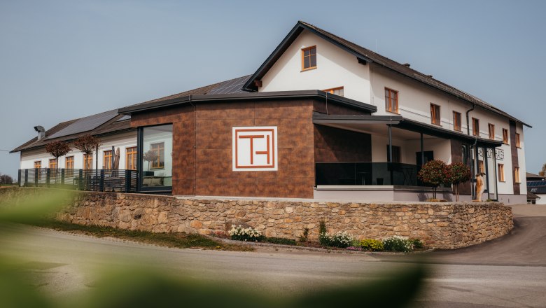 Moderná budova s označením "Gasthof Thaler", obklopená kamenným múrom a rastlinami.