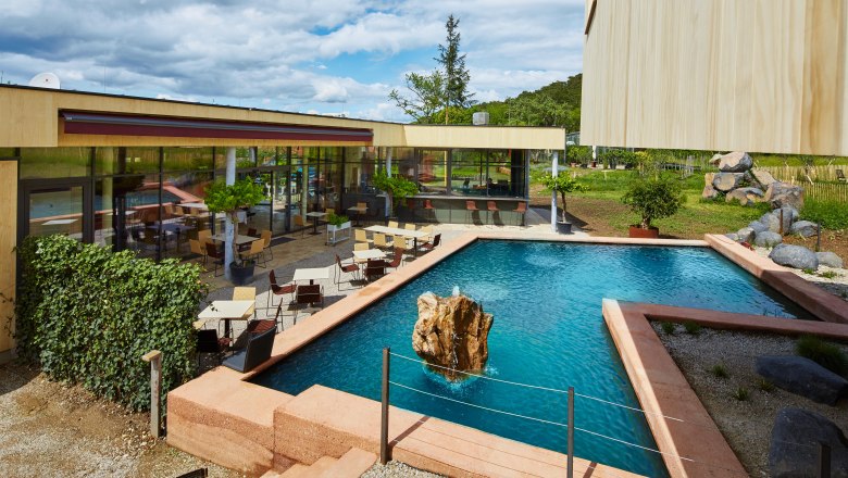 Moderná terasa so stolmi a stoličkami pri obdĺžnikovom jazierku so skalami uprostred.