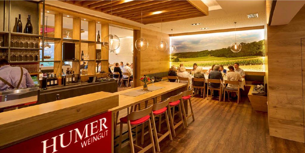 Pohľad do interiéru modernej vinárne s dreveným nábytkom a veľkou fototapetou vinohradu.