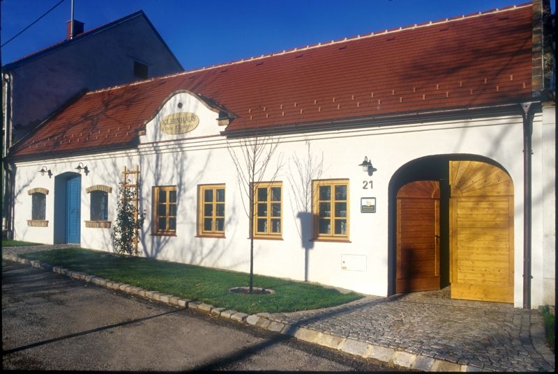 Biela budova s červenou strechou a drevenými dverami s označením "Kleinhaus".