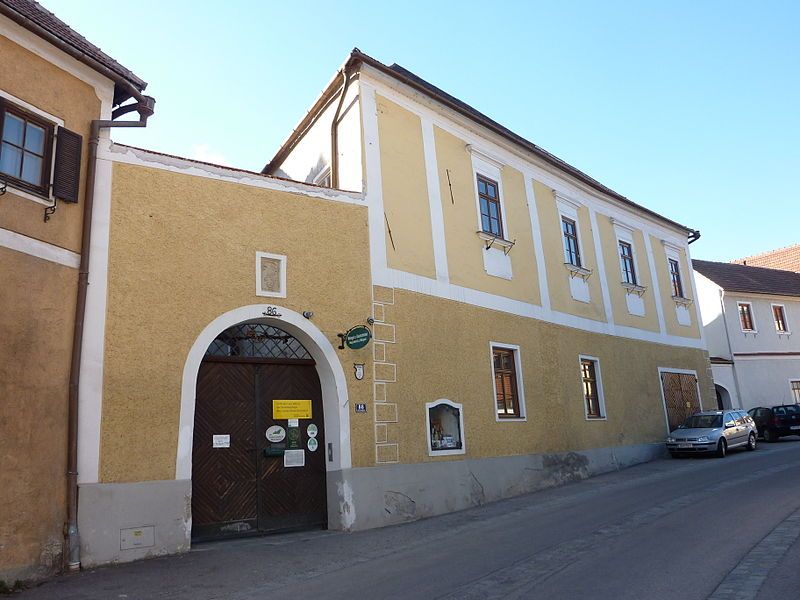 Žltá dvojpodlažná budova s drevenou bránou a oknami na ulici.