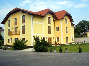 Žltá dvojpodlažná budova s červenou strechou a udržiavanou záhradou.