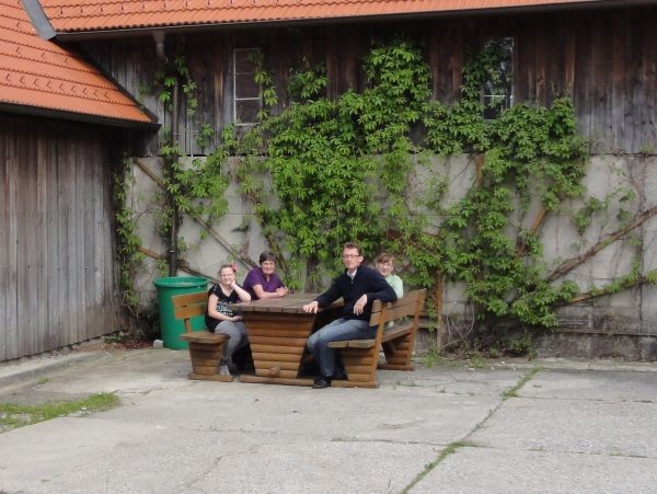 Štyria ľudia sedia pri drevenom stole pred budovou obrastenou brečtanom.