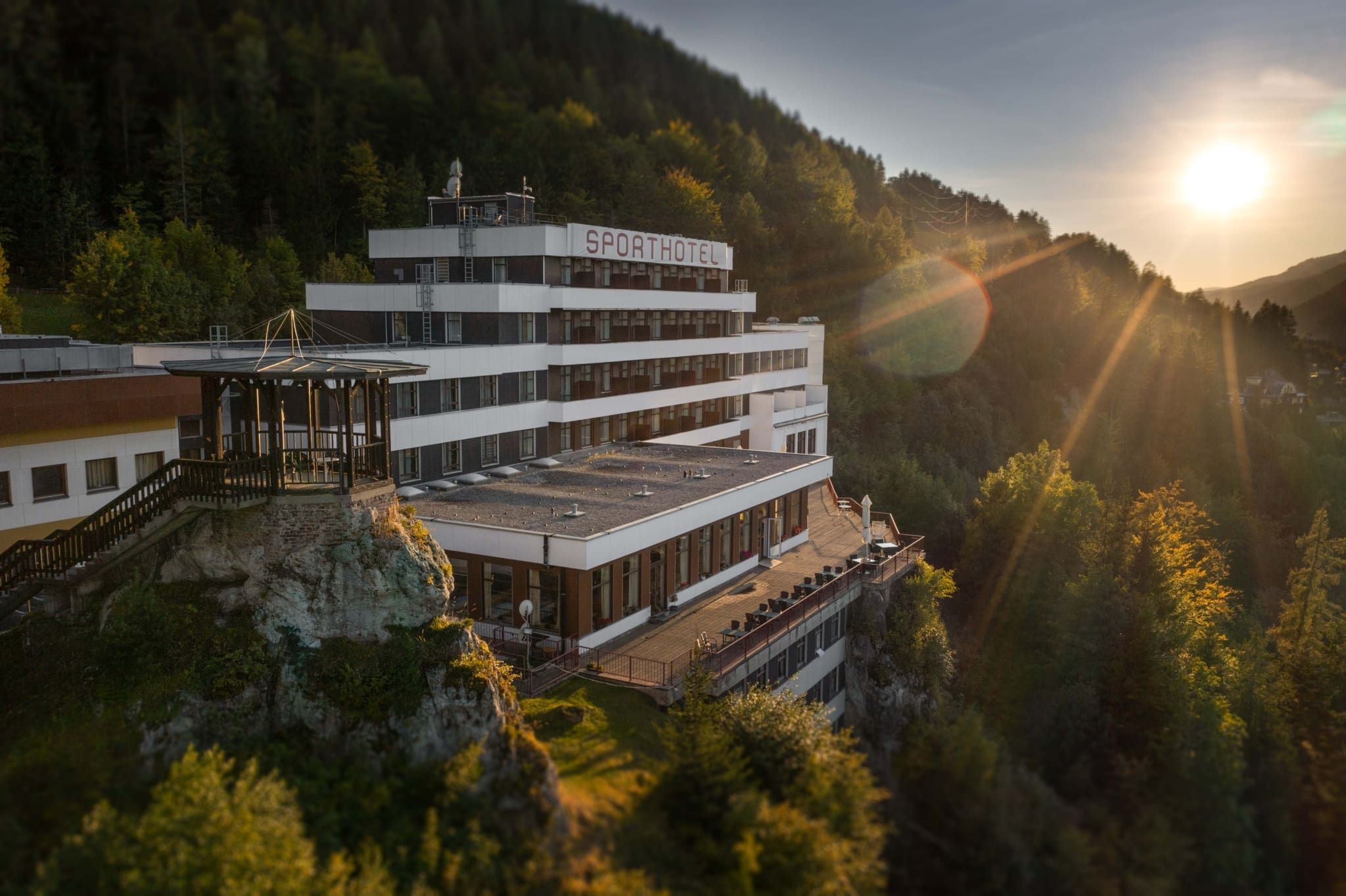 Hotel na kopci pri západe slnka, obklopený lesom.