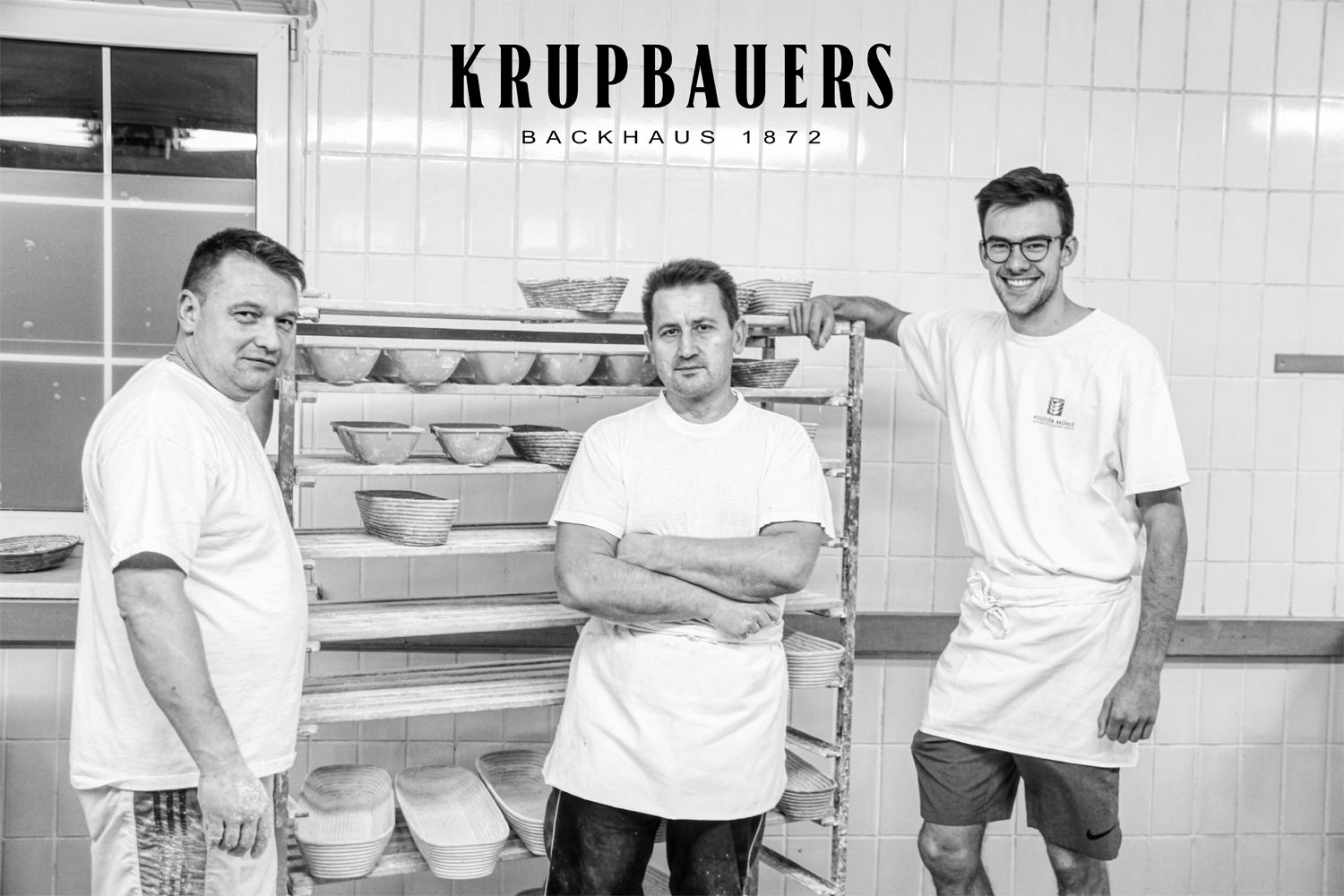 Traja pekári v pekárni s košíkmi na chlieb v pozadí.