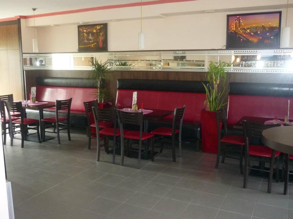 Pohľad do interiéru kaviarne s červenými lavicami a čiernymi stoličkami.