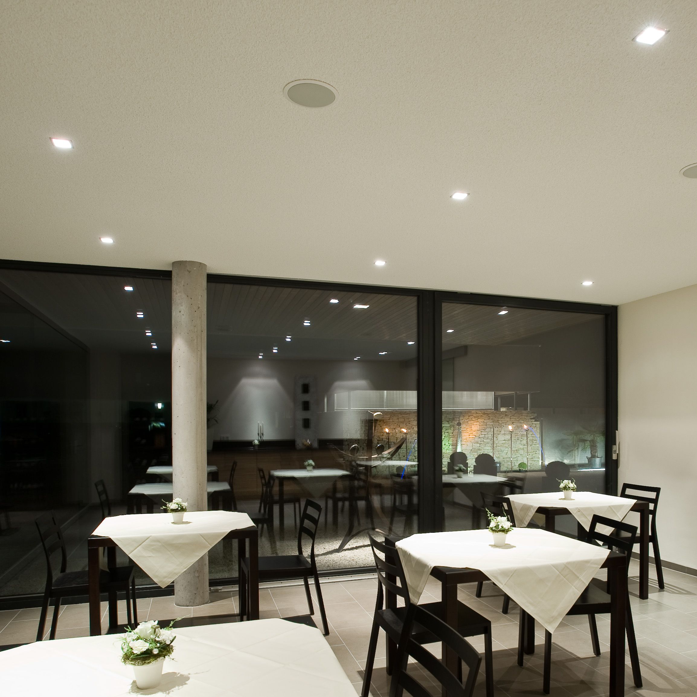 Moderná raňajková miestnosť so stolmi a stoličkami, zdobená bielymi obrusmi a kvetmi.