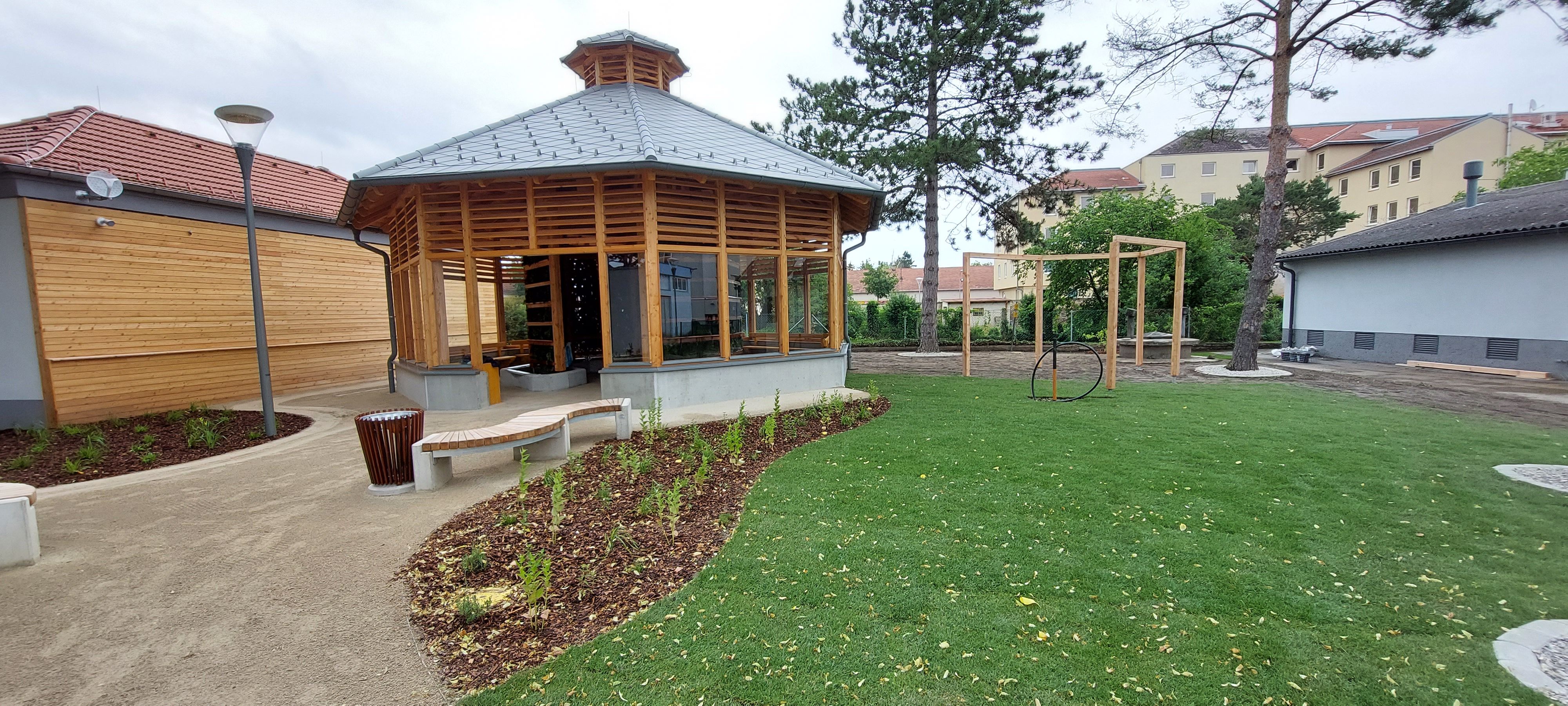 Moderné inhalatórium s drevenou konštrukciou a sklenenými oknami v udržiavanej záhrade s trávnikom a stromami.