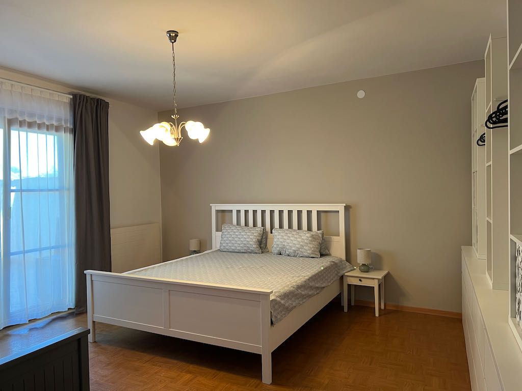 Spálňa s bielou posteľou, nočným stolíkom a šatníkovou skriňou.