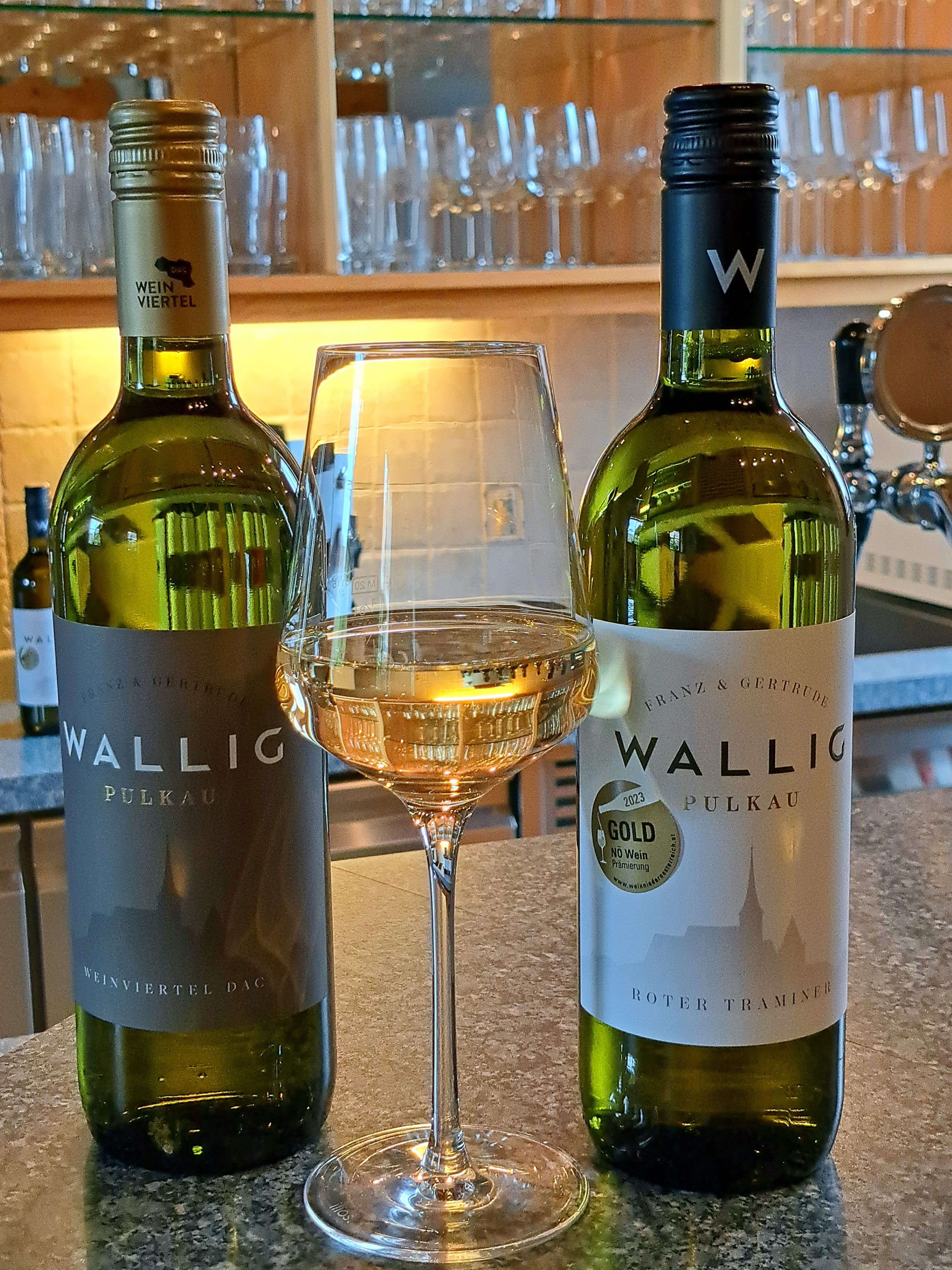 Dve fľaše vína a pohár bieleho vína na pulte.