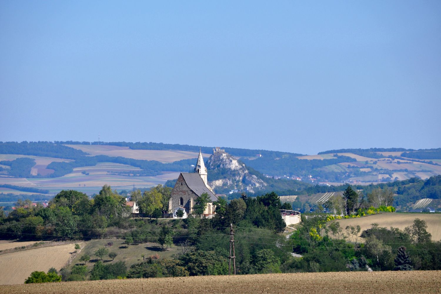 Krajina s kostolom a kopcom v pozadí.