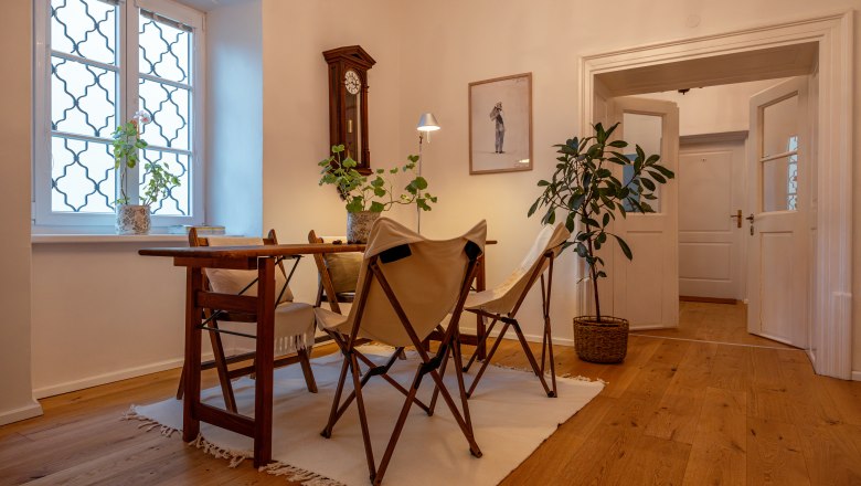 &Uacute;tuln&aacute; izba s drevenou podlahou, stolom, stoličkami a rastlinami.