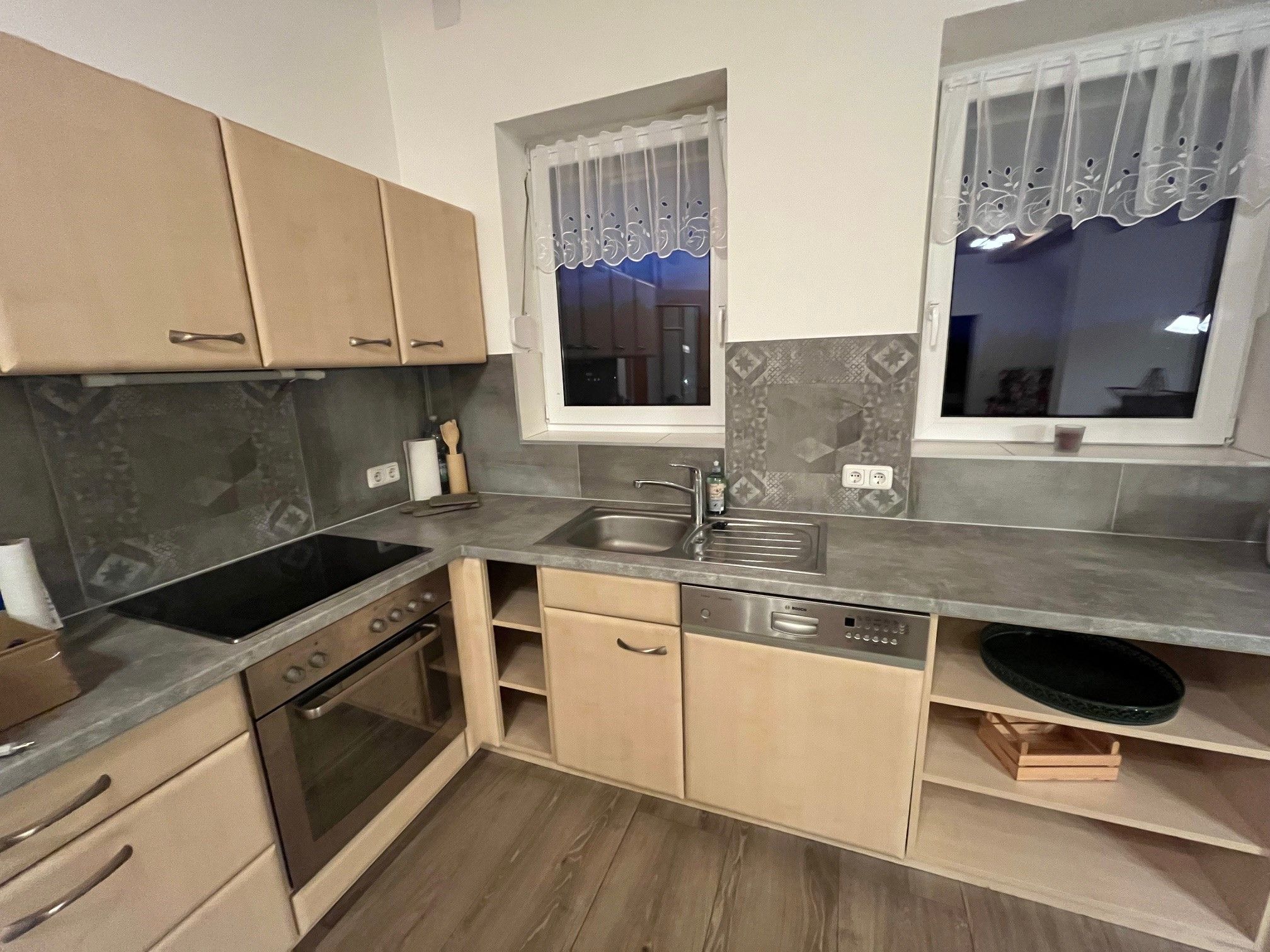 Moderná kuchyňa s drevenými skrinkami, elektrickým sporákom, drezom a umývačkou riadu.