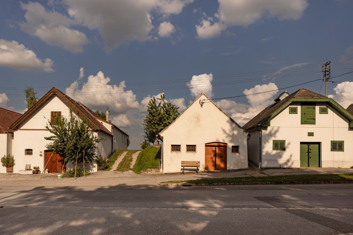 Tri tradičné pivničné domy v Kettlasbrunne pod modrou oblohou s mrakmi.