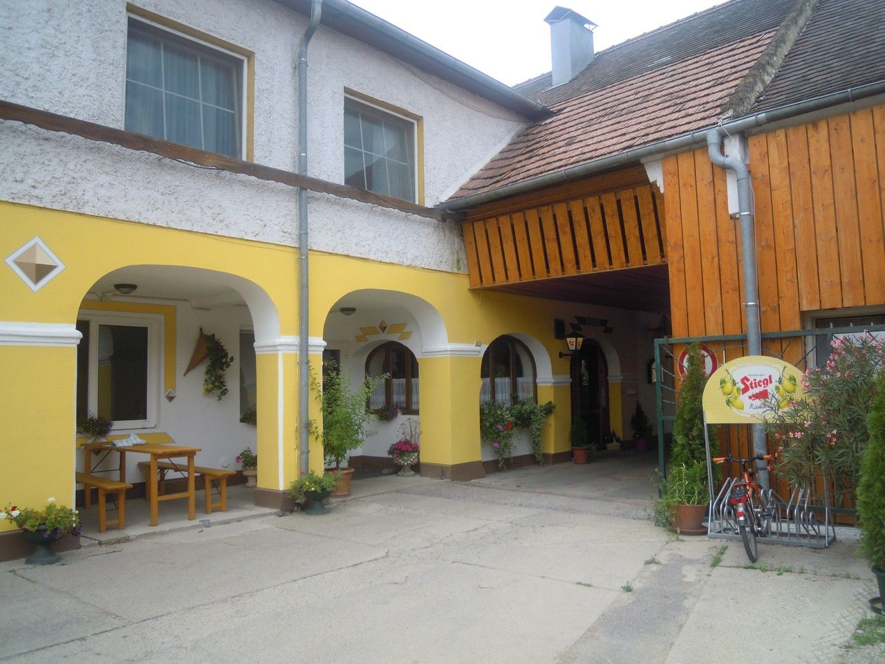 Žlté arkádové nádvorie s drevenou strechou a rastlinami.