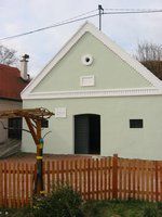 Malá, svetlozelená budova so šikmou strechou a dreveným plotom pred ňou.