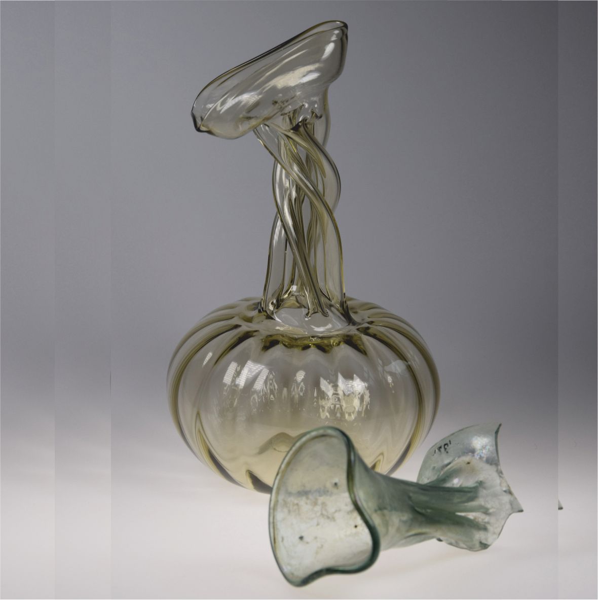 Sklenený objekt s pokrútenými tvarmi na sivom pozadí.