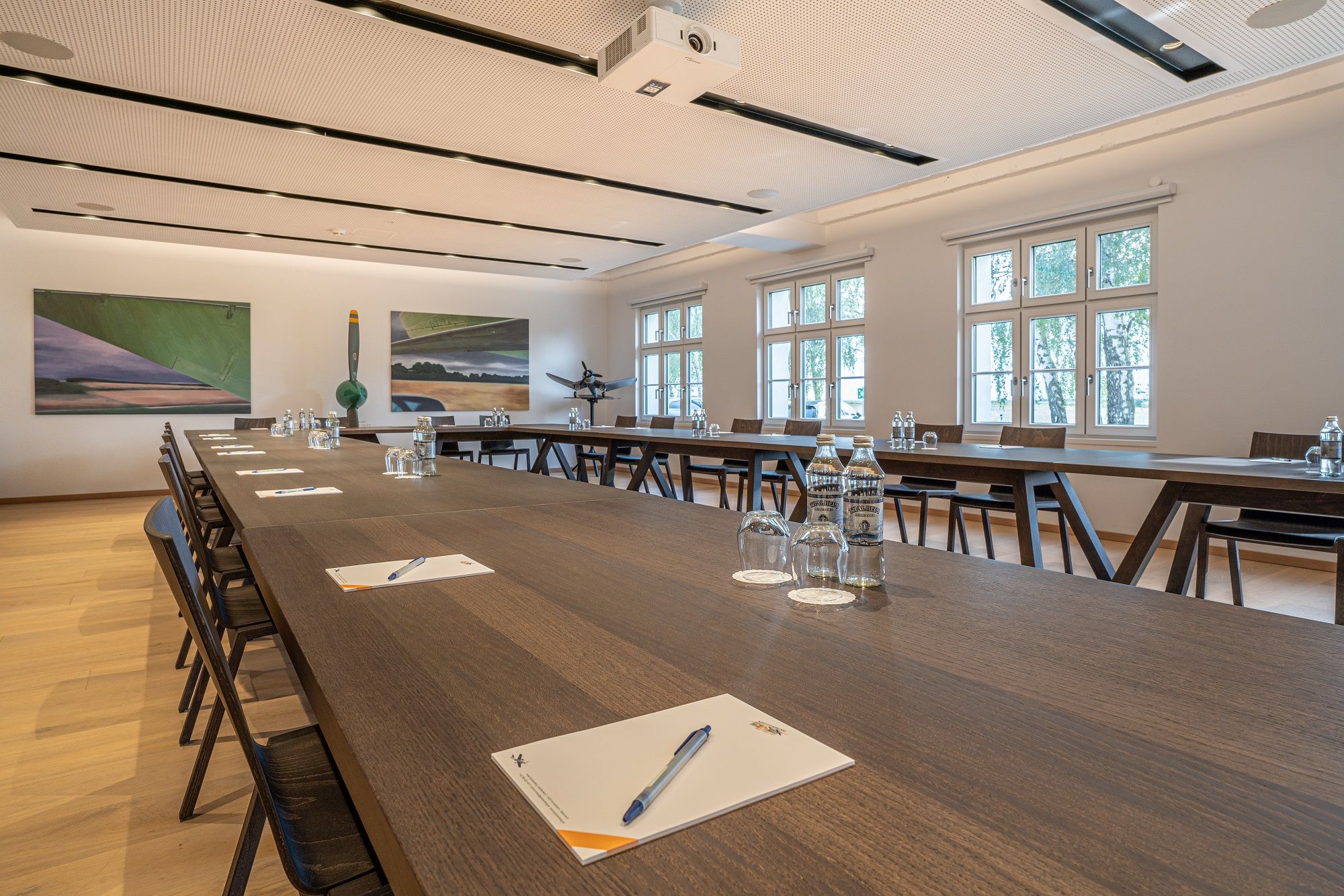 Seminárna miestnosť v hoteli Spitzerberg s dlhými drevenými stolmi, stoličkami, fľašami na vodu a písacími potrebami.