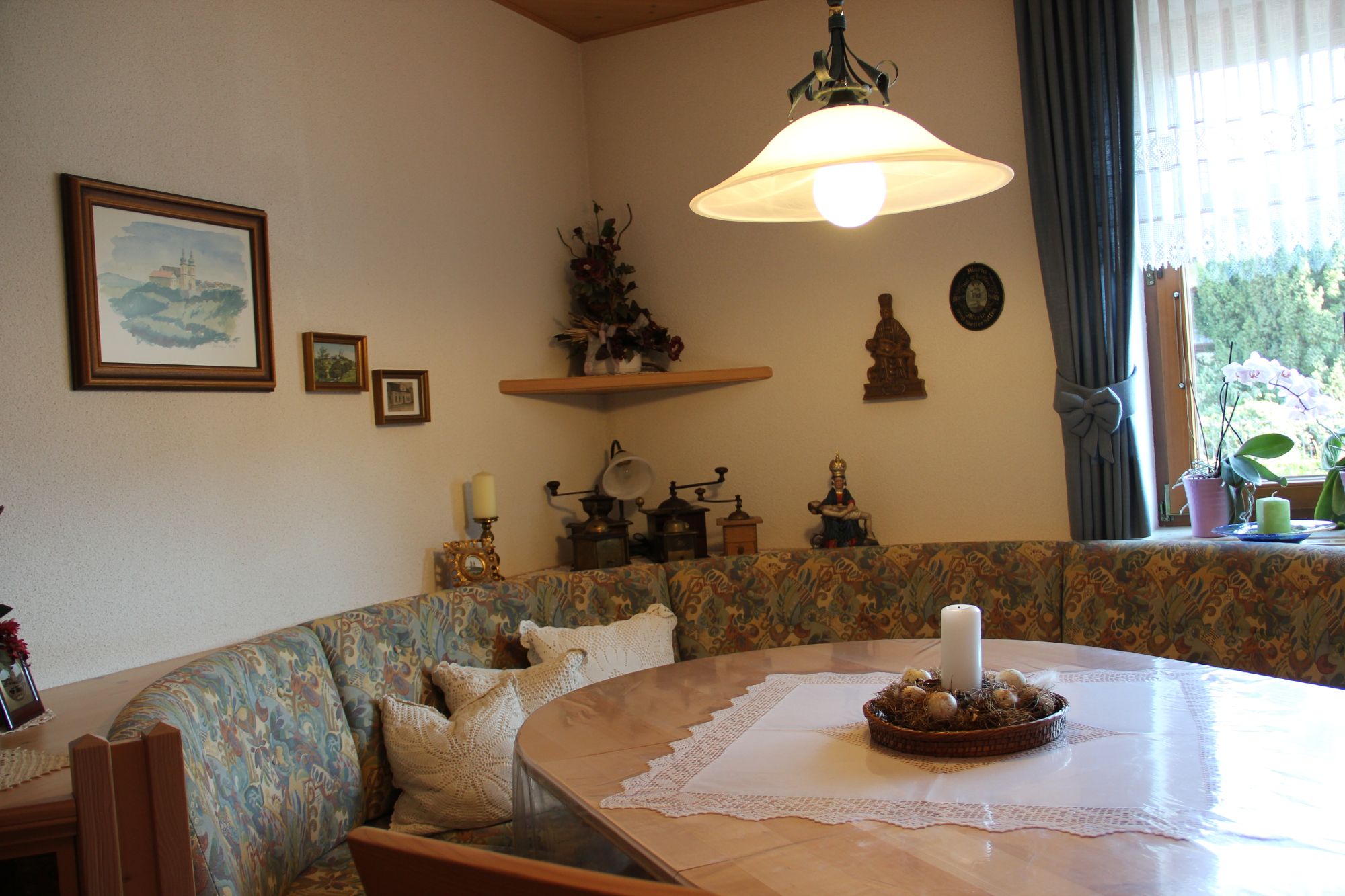 Útulná raňajková miestnosť s rohovou lavicou, stolom, sviečkou a dekoráciami na stene.