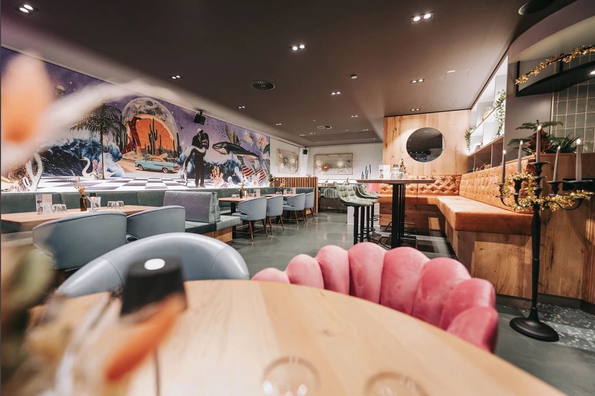 Pohľad do interiéru štýlovej reštaurácie s moderným nábytkom a umeleckými dielami na stenách.