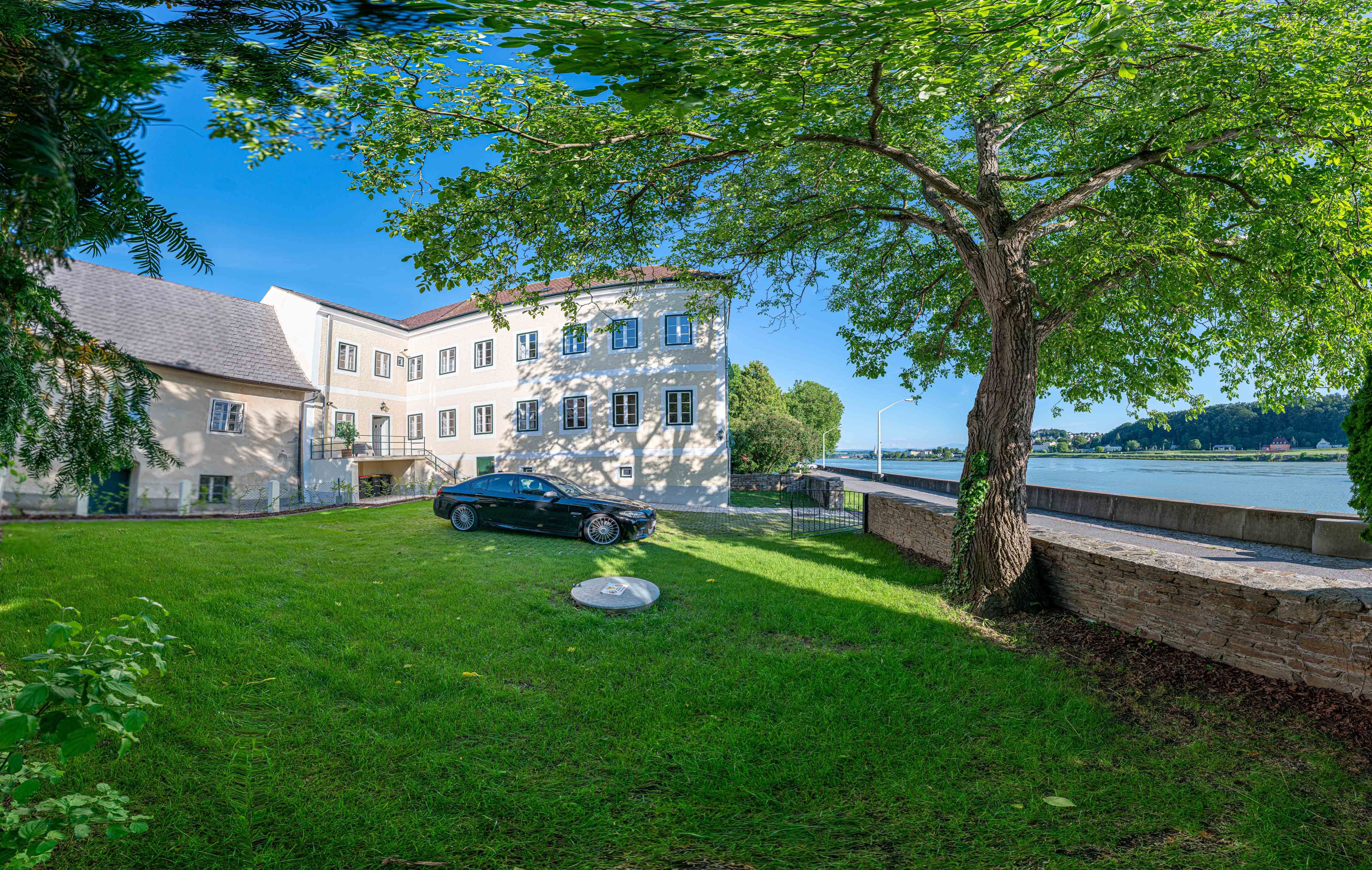 Exteriérový pohľad na starú poštu so stromom a autom v popredí, v pozadí Dunaj.