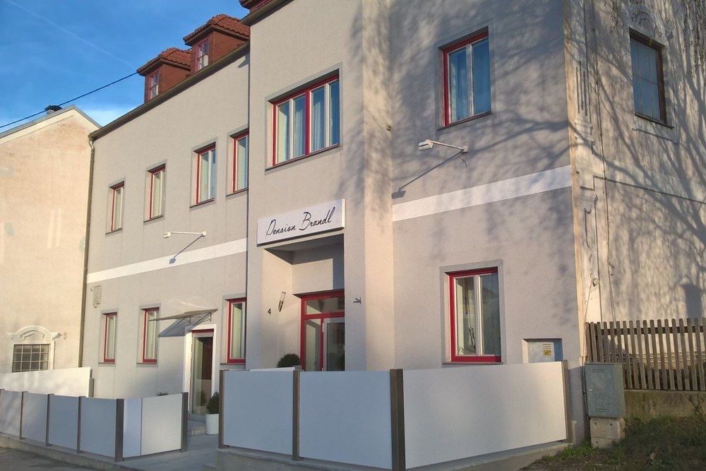Exteriérový pohľad na penzión Brandl so sivou fasádou a červenými okennými rámami.