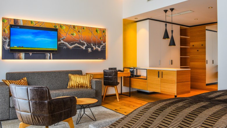 Modern&aacute; hotelov&aacute; suita s pohovkou, kreslom, TV a kuchynsk&yacute;m k&uacute;tom.