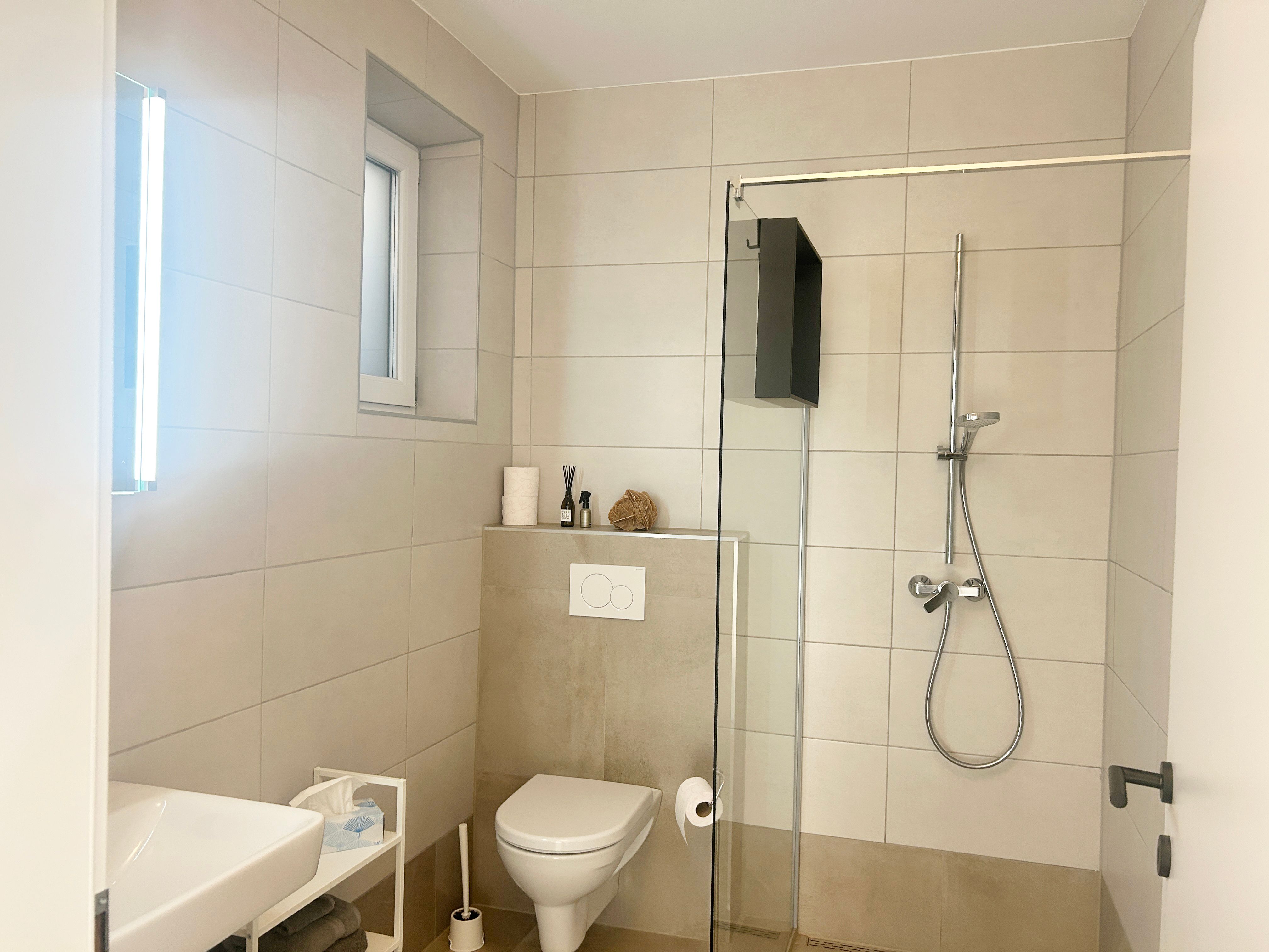 Moderná kúpeľňa so sprchovacím kútom, WC a umývadlom.
