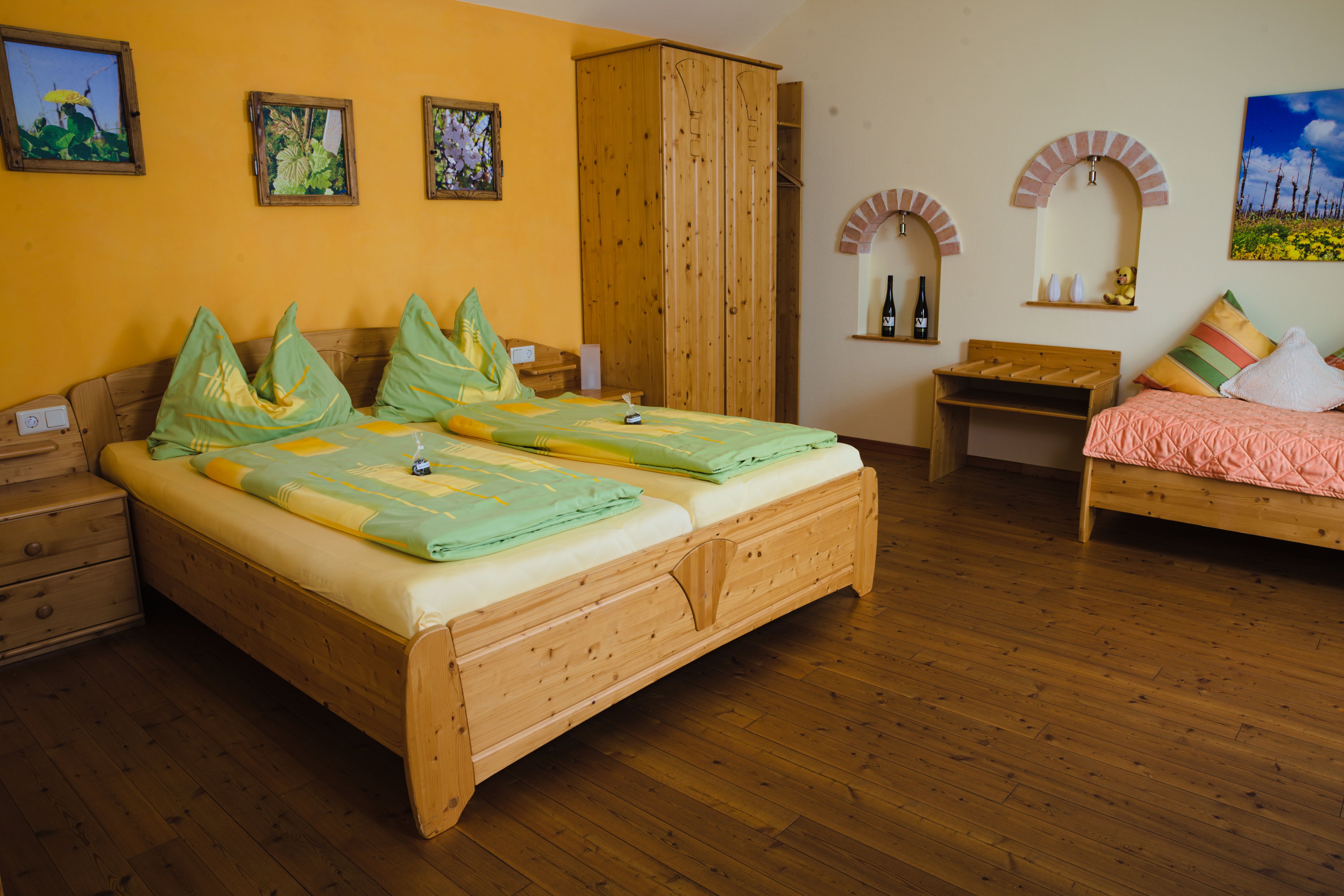 Útulná izba pre hostí s dreveným nábytkom, manželskou posteľou, samostatným lôžkom a dekoratívnymi obrázkami na stene.