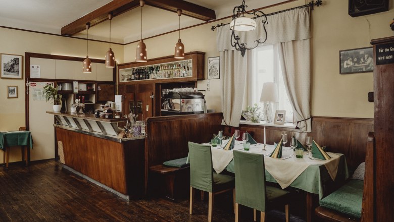 &Uacute;tuln&aacute; kaviareň s dreven&yacute;m n&aacute;bytkom, prestret&yacute;m stolom a barov&yacute;m pultom.