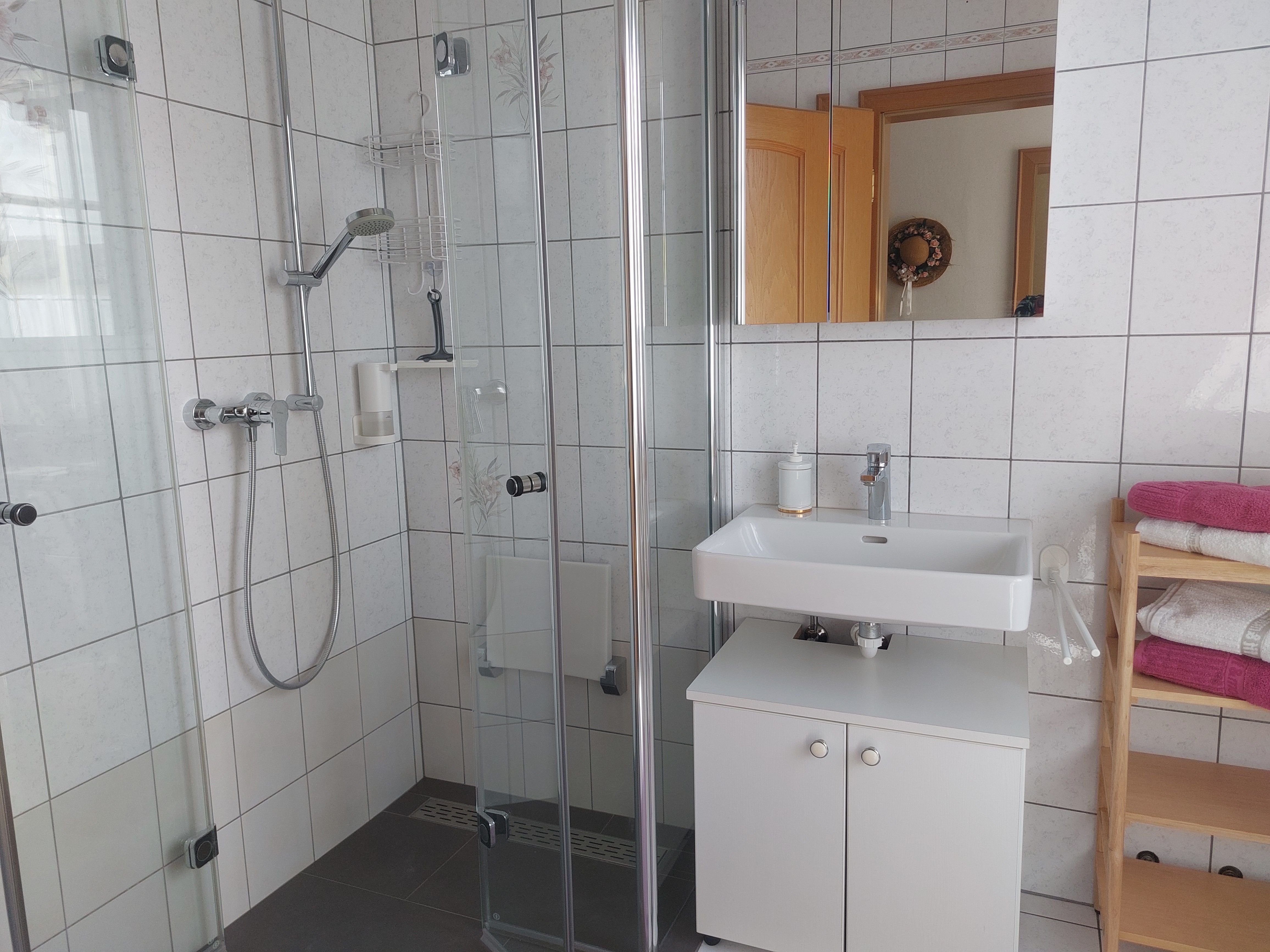 Moderná kúpeľňa so sprchovacím kútom, umývadlom a vešiakom na uteráky.