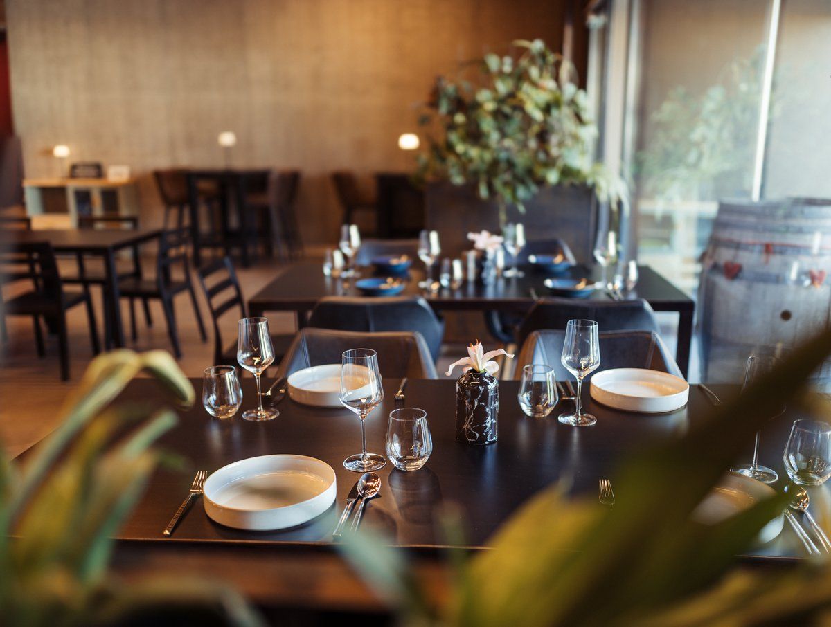 Elegantná reštaurácia s prestretými stolmi, pohármi na víno a rastlinami v pozadí.