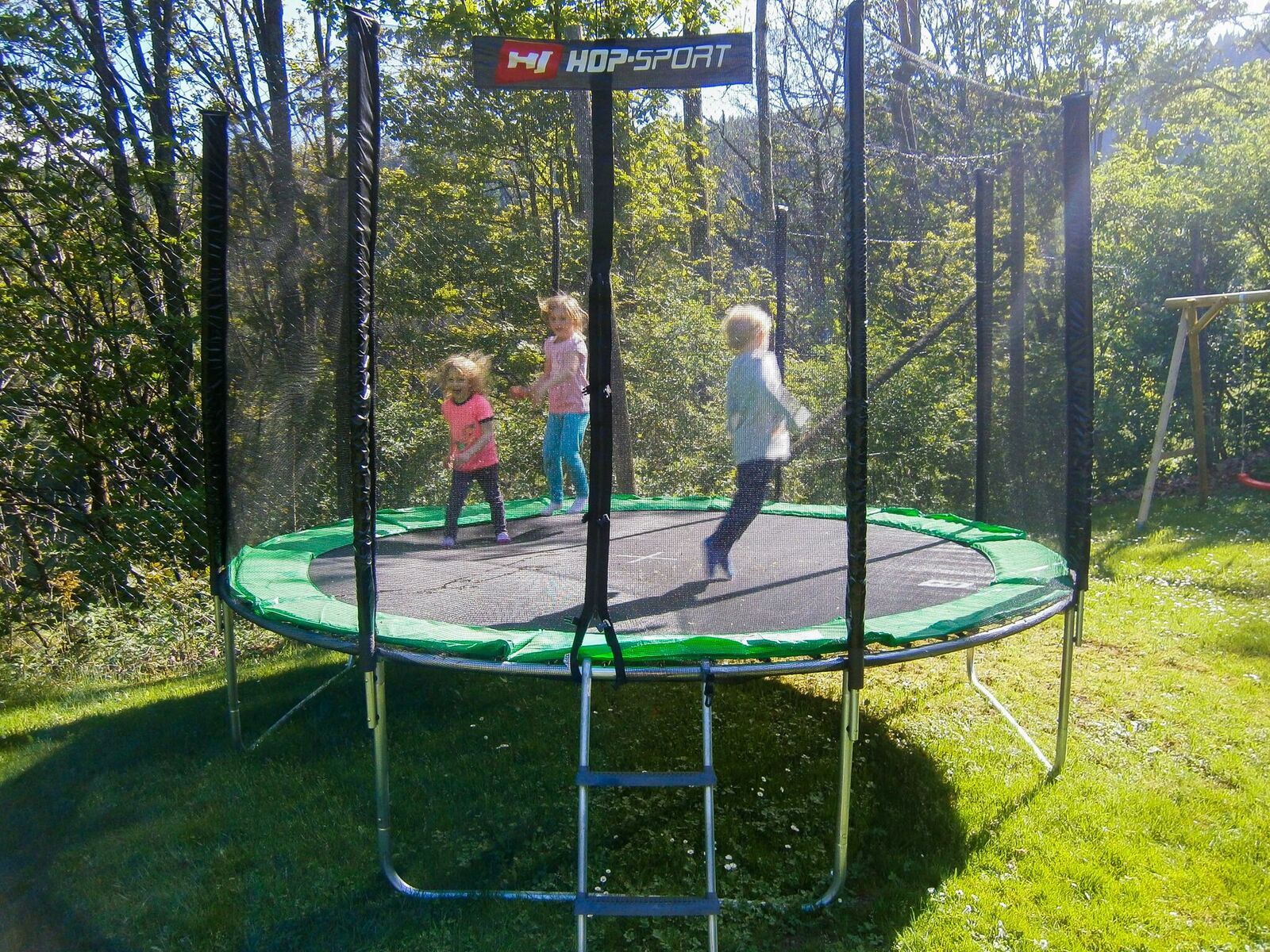 Tri deti skáču na trampolíne vonku.