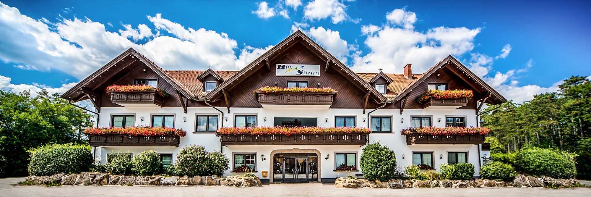Tradičný hotel s drevenými balkónmi a kvetinovými truhlicami na pozadí modrej oblohy.