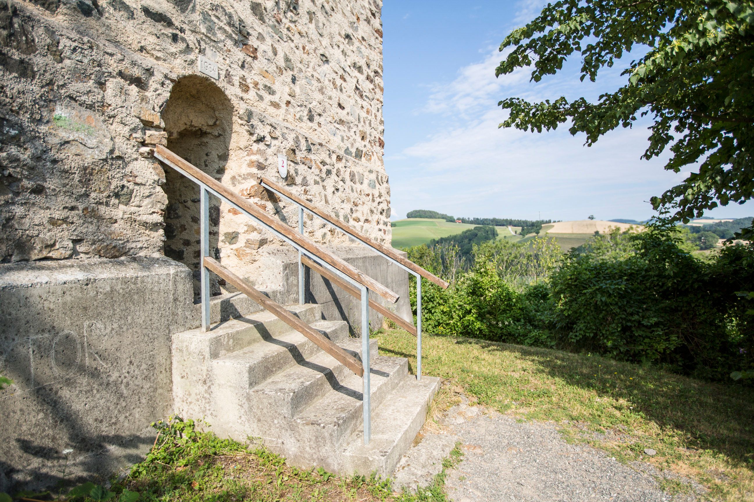 Vchod do požiarnej veže zrúcaniny hradu Kirchschlag so schodiskom a krajinou v pozadí.