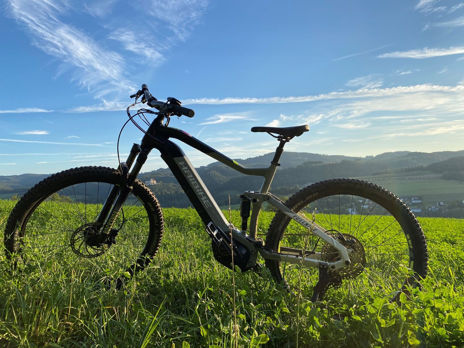 Detailný záber na bicykel na zelenej lúke s kopcovitou krajinou v pozadí.