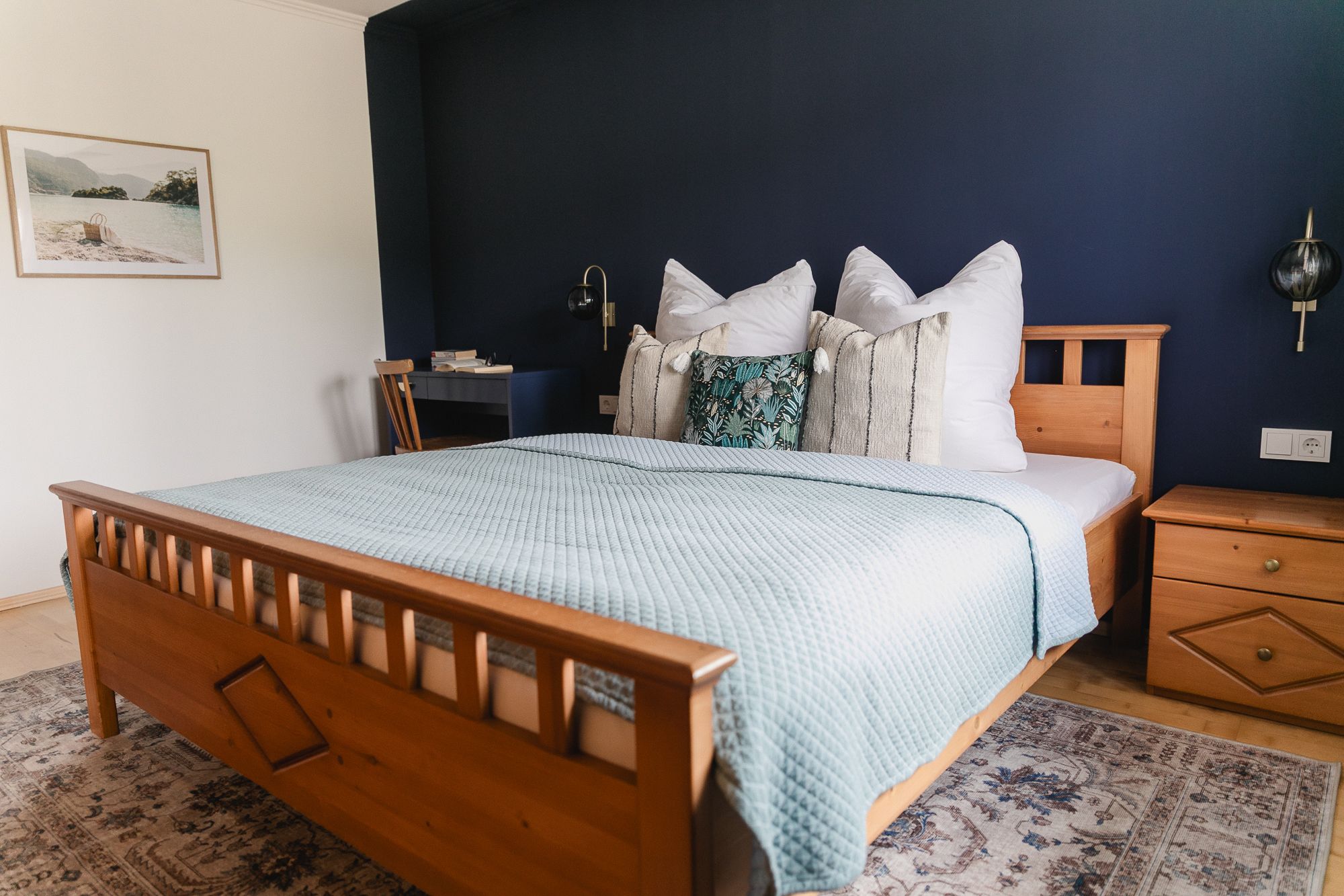 Útulná spálňa s drevenou posteľou, modrou stenou a ozdobnými vankúšmi.