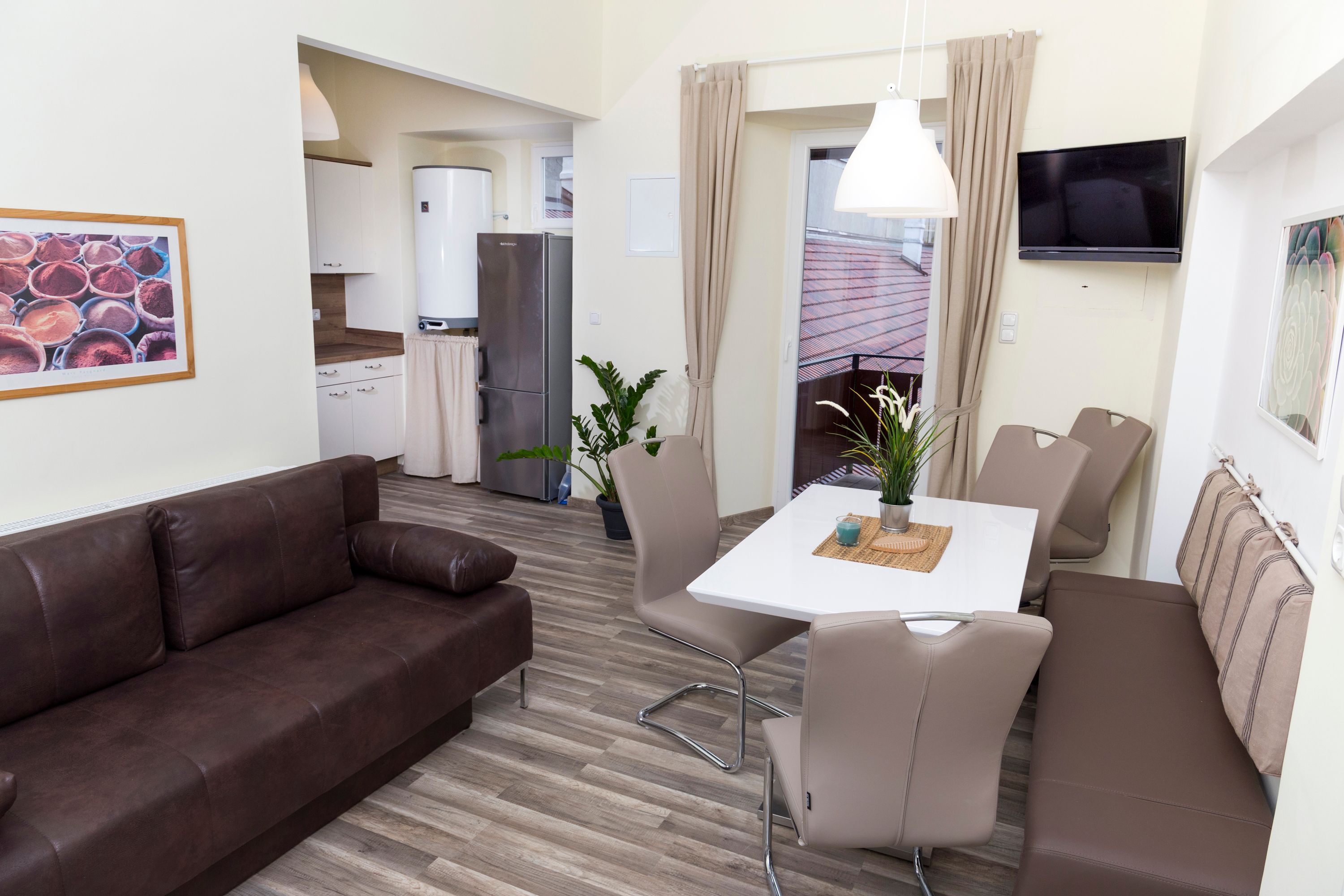 Moderná kuchyňa s hnedou pohovkou, jedálenským stolom a stoličkami, chladničkou a rastlinami.