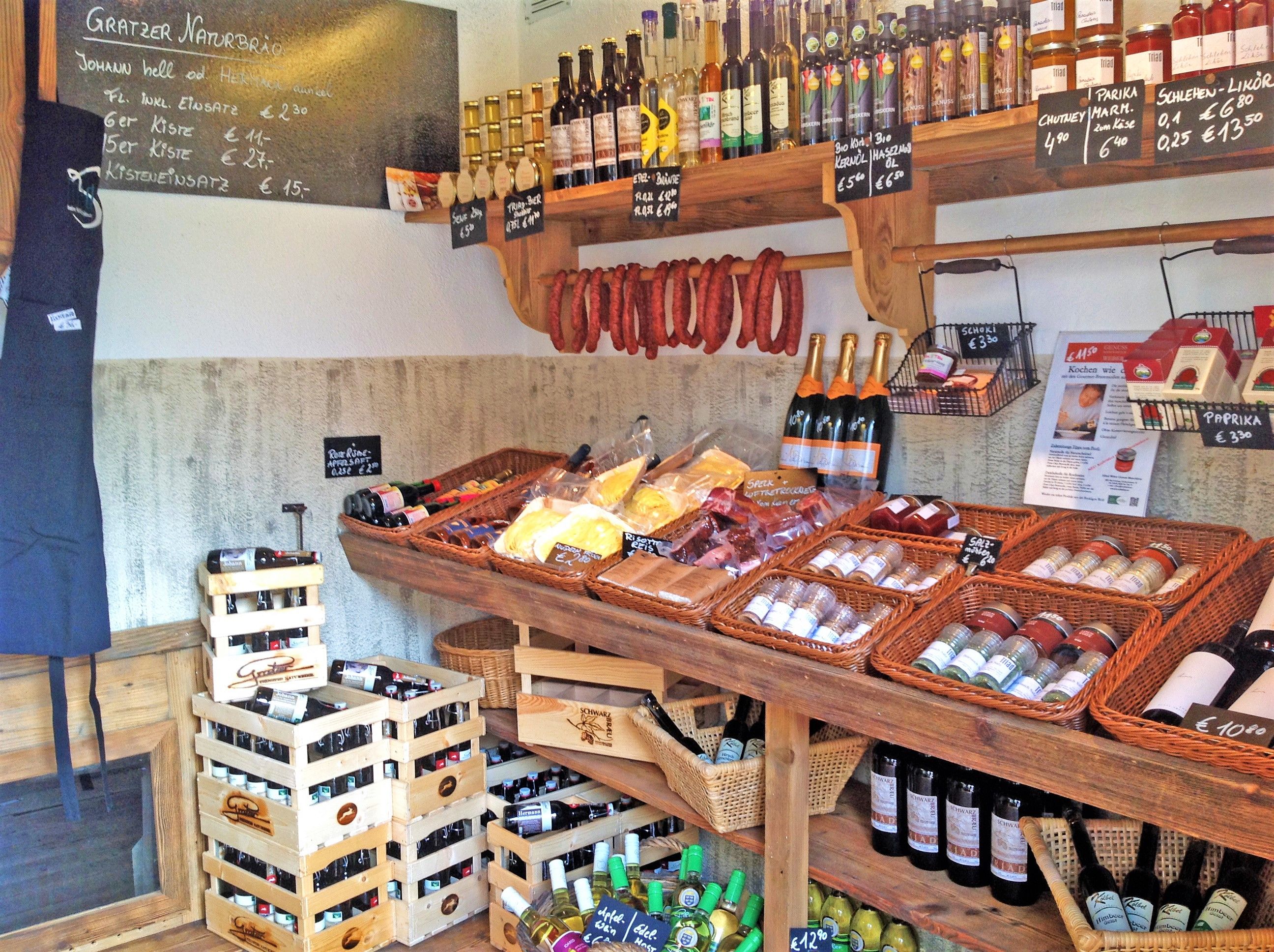 Pohľad do interiéru farmárskeho obchodu s regálmi plnými regionálnych produktov, ako je víno, klobásy, korenie a olej.