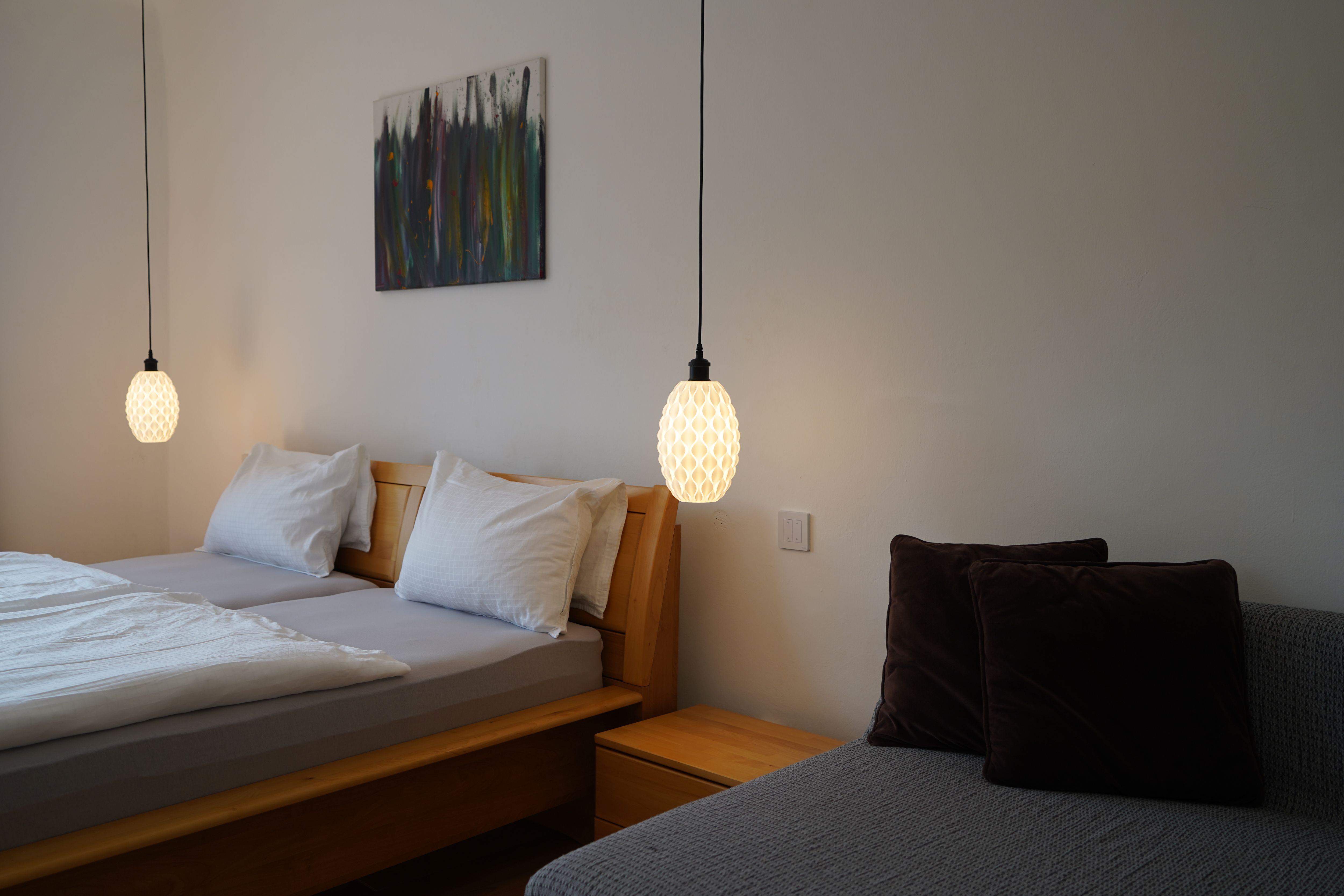 Spálňa s manželskou posteľou, dvoma závesnými lampami a pohovkou s vankúšmi.