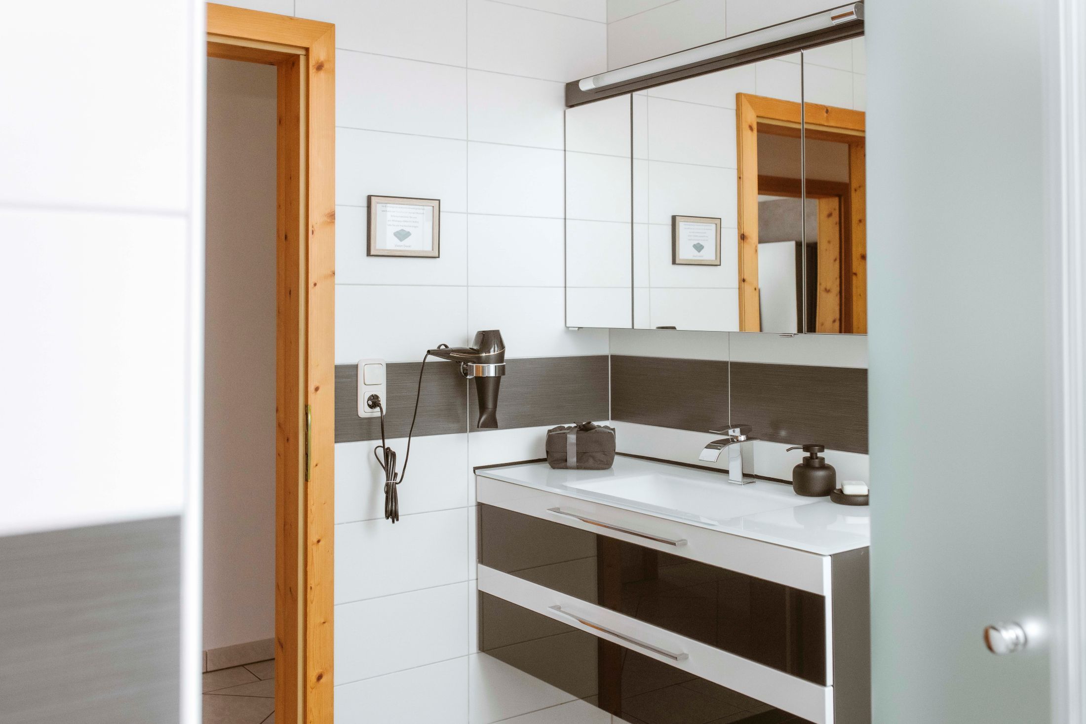 Moderná kúpeľňa so zrkadlom, umývadlom a sušičom vlasov na stene.