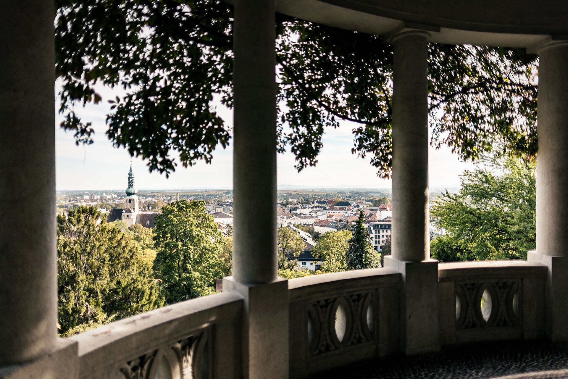 Von dieser malerischen Aussichtsplattform aus eröffnet sich ein atemberaubender Blick über die sanften Hügel und die charmante Stadt. Die üppigen Bäume spenden Schatten und laden dazu ein, die Ruhe der Natur zu genießen. Ein perfekter Ort, um die Seele baumeln zu lassen und die Schönheit der Umgebung zu erleben.