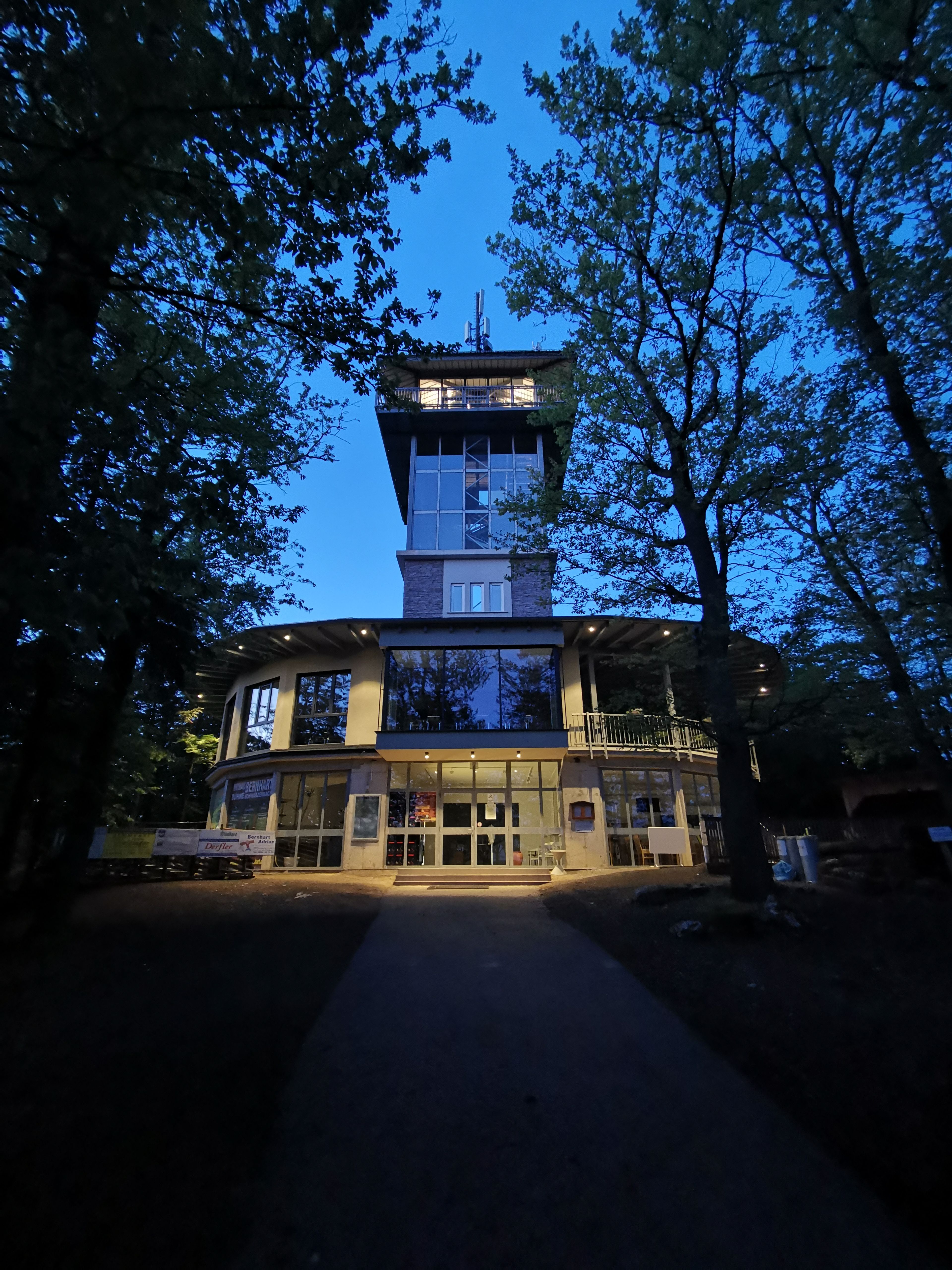 Oválna budova so sklenenou vyhliadkovou vežou v noci.