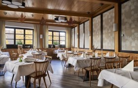 Elegantná reštaurácia s dreveným nábytkom, bielymi obrusmi a veľkými oknami s jesennými stromami.