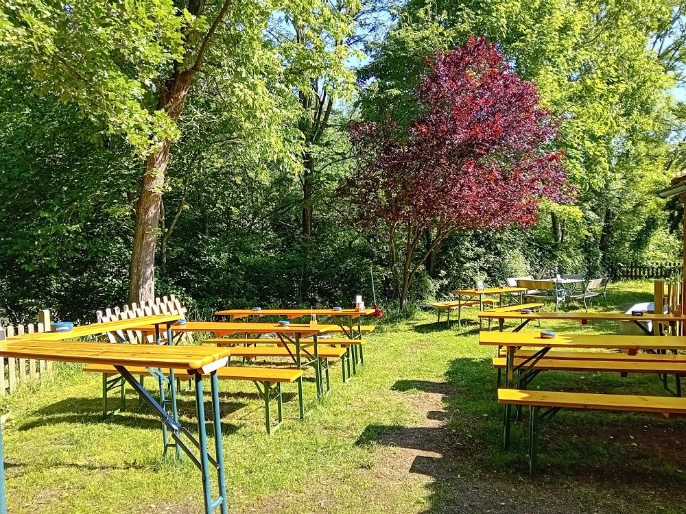 Pivná záhrada s prázdnymi drevenými lavicami a stolmi pod stromami.