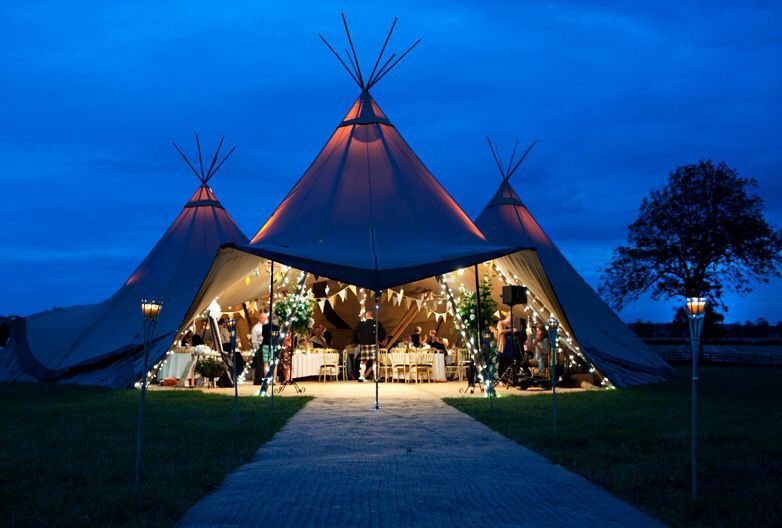 Osvetlený stan tipi v noci so slávnostnou výzdobou a hosťami vo vnútri.