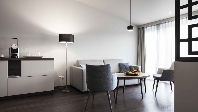 Modern&yacute; priestor na sedenie s pohovkou, kreslom, stolom a stojacou lampou vo svetlej miestnosti.